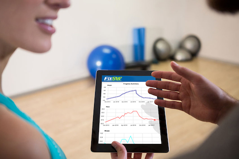 Personal Trainer Viewing Client's Fitness Progress Graphs Personal Trainer with client looking at tablet displaying client fitness progress graphs while working out.